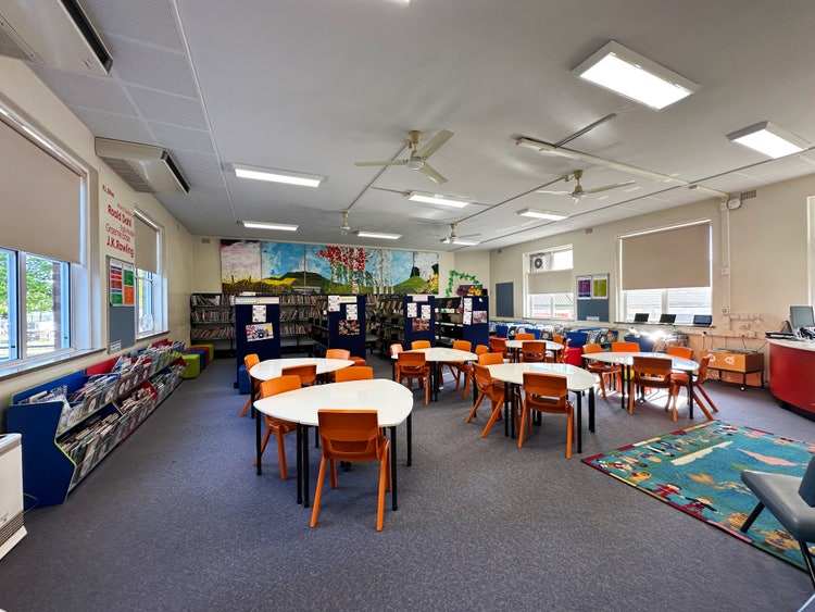 A picture of the inside of our Library showing chairs and tables and shelves of books.