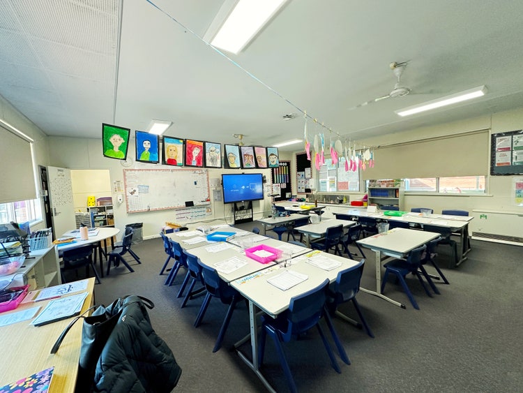 Inside a classroom showing desks, smartboard, art hanging and teachers desk.