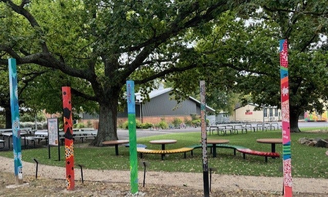 A photo of our totem poles and curved seats in the sensory garden with large green trees shading the area.