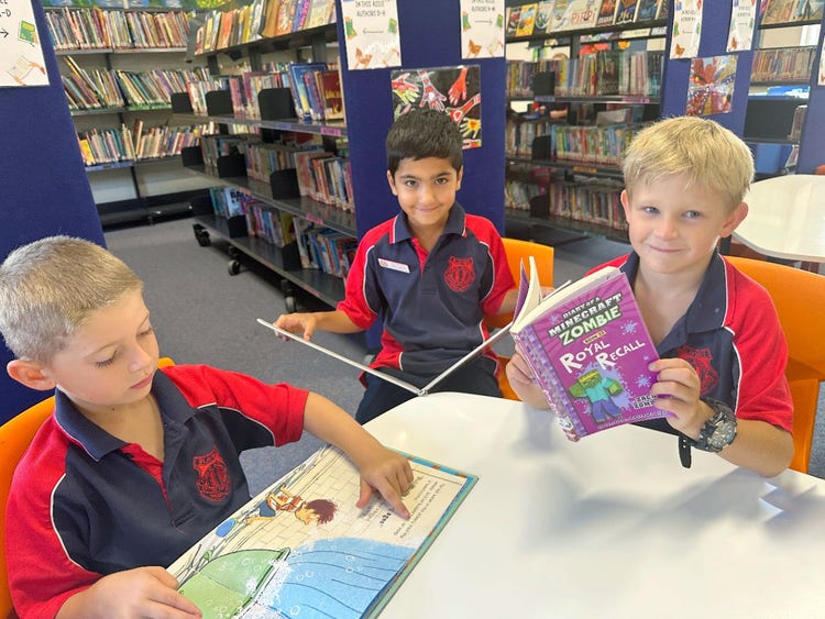 Three boys sitting in the library reading books.