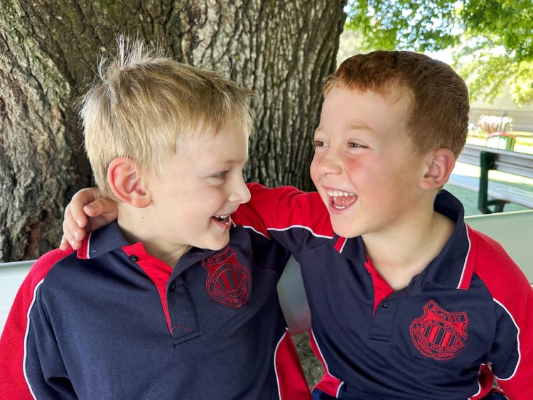 Two boys laughing with arms around each other sitting on bench seat.